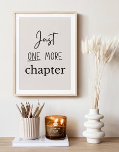 there is a candle and some flowers on the table next to a framed poster that says just one more chapter