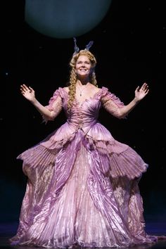 a woman in a purple dress standing on a stage with her hands out to the side