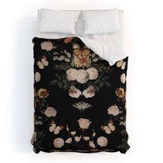 a bed with black and white floral comforter set on it's side, along with two pillows