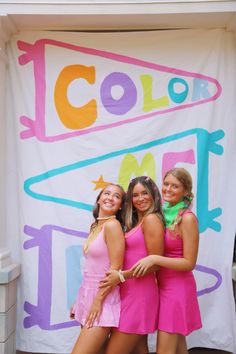 three girls are posing in front of a colorful sign