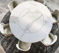 a white marble dining table surrounded by chairs and an area rug that looks like wood