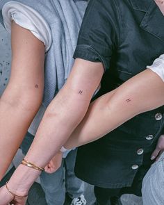 two people holding hands with small tattoos on their arms and wristbands, while one person holds the other's hand