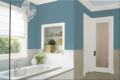 a bathroom with blue walls and white trim, including a chandelier above the bathtub