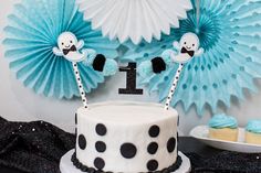 a birthday cake decorated with black and white polka dot icing, two ghost toppers and one letter i