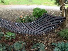 a wooden hammock sitting next to a tree in the grass and plants around it