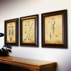 three framed art pieces on the wall above a wooden desk with golf clubs and tees