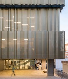 two people are walking in front of a building with vertical blinds on the side of it