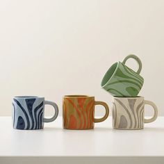 three coffee mugs sitting next to each other on a white counter top, one has a green and blue design on it