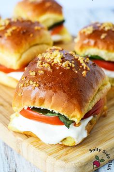 three sandwiches on a cutting board with cheese and tomatoes in the middle, topped with bread crumbs