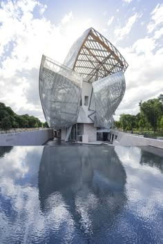 an artistic building with a large metal structure on it's roof and water in the foreground