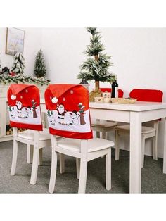 two white chairs sitting at a table with christmas decorations on it and a red santa clause chair cover