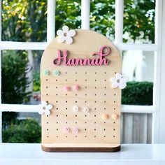 a wooden peg board with flowers and the word hannah written in pink on it next to a window