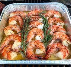 cooked shrimp with rosemary on top in an aluminum baking pan, cooking over an open grill