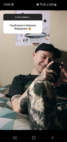 a man sitting on top of a bed holding a cell phone in his hand and smiling