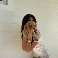 a woman holding a small dog up to her face while standing in front of a house