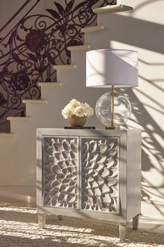 a table with a lamp and vase on it next to a stair case that has an intricate design