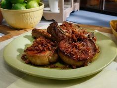 a green plate topped with meat covered in sauce next to a bowl of lemons