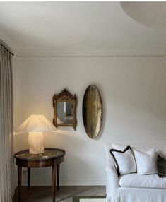 a living room with a couch, table and two mirrors on the wall above it