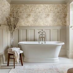 a white bath tub sitting in a bathroom next to a wooden stool and wall paper