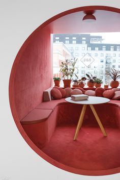 a room with pink walls and plants in the corner, as seen through a circular window