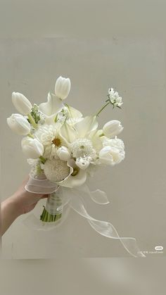 a bouquet of white flowers is held by a person's hand in front of a wall