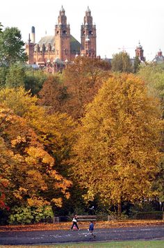 two people are walking through the park in autumn