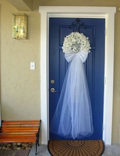 a blue front door with a white wedding dress and flowers on it, next to a bench