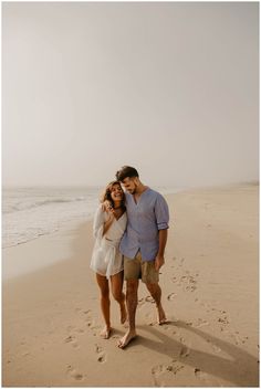 a man and woman standing on top of a sandy beach next to the ocean with footprints in the sand