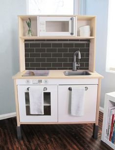 a toy kitchen with sink, stove and microwave on it's shelf next to a window