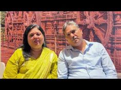 a man and woman sitting next to each other in front of a wall with carvings on it