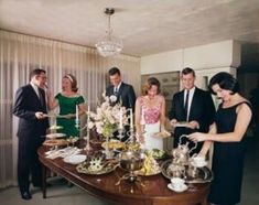 a group of people standing around a table with food on it