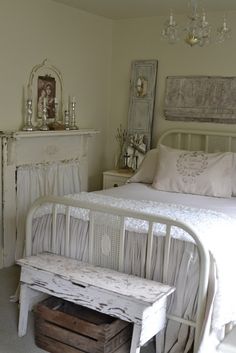 a white bed sitting under a chandelier next to a wooden dresser and mirror