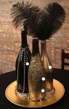 three wine bottles are sitting on a gold plate with pearls and feathers in the top