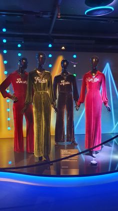 four mannequins dressed in velvet outfits stand on a stage with brightly colored lights behind them