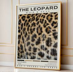 a leopard print on the wall next to a white and gold framed poster that reads, the leopard wild's sky