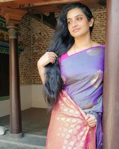 a woman in a purple and pink sari standing next to a brick building with columns