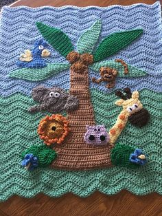 a crocheted blanket with animals and palm tree on it, sitting on a wooden table