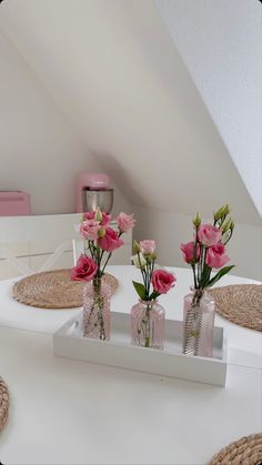 three vases filled with pink flowers sitting on top of a white table in a room