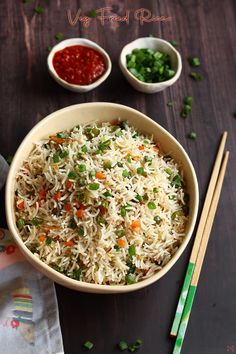 a bowl filled with rice and vegetables next to chopsticks on a wooden table