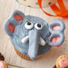 an elephant cupcake with pink frosting and eyes on it, surrounded by other cupcakes