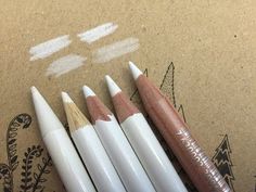 four pencils sitting next to each other on top of a piece of brown paper