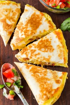 four slices of quesadilla sitting on top of a wooden cutting board next to a bowl of salad