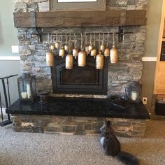 a cat sitting on the floor in front of a fire place with mugs hanging above it