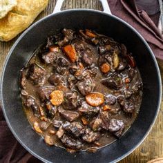 a pan filled with meat and vegetables on top of a wooden table next to chips