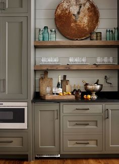 a kitchen with gray cabinets and shelves filled with bottles, glasses, and other items