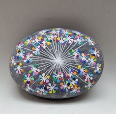 a rock with flowers painted on it sitting in front of a gray wall and grey background