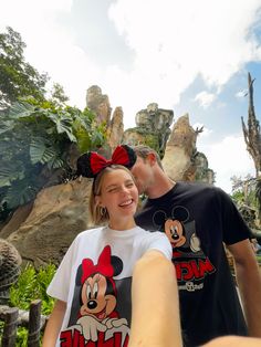 a man and woman standing next to each other in front of a rock formation at disney world