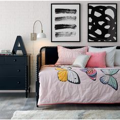 a bed with pink sheets and pillows in a room next to two framed pictures on the wall