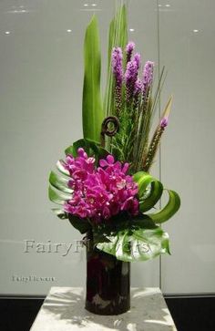 a vase filled with purple flowers on top of a white tablecloth covered floor next to a glass wall