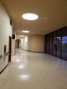 an empty hallway with glass doors and lights on the wall, in front of large windows